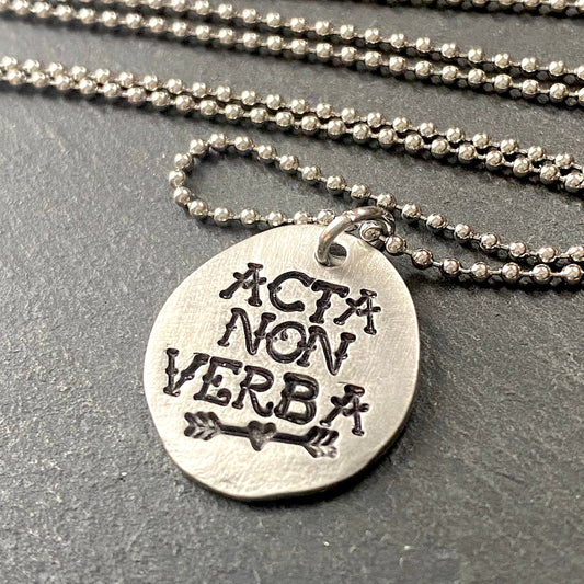 acta non verba latin phrase necklace.  deeds not words hand stamped in tattoo font in pewter disc with heart arrow. drake designs jewelry